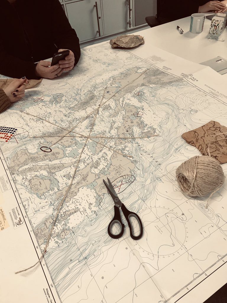 Photo of a map with string lines across it next to a pair of scissors and ball of string.