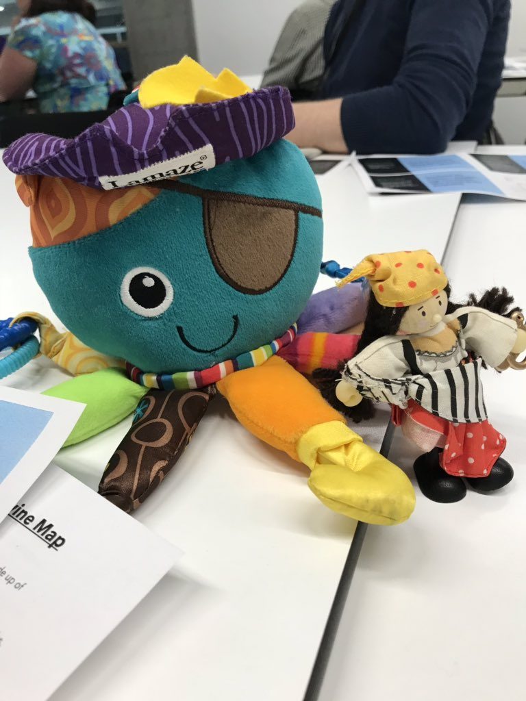Photo of a colourful toy octopus on a desk with people and paperwork behind.