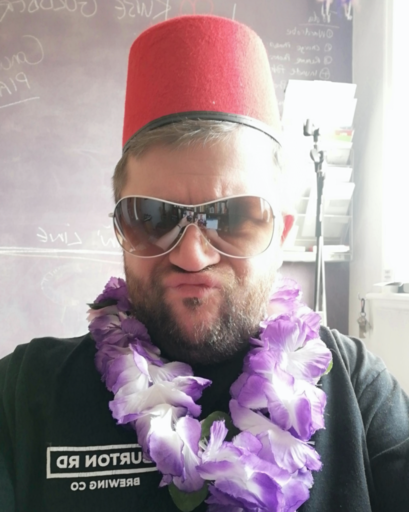 James Charnock in a Fez and sunglassse and wearing a Lei