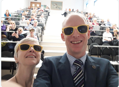Photo of conference with delegates and two presenters all wearing sunglasses