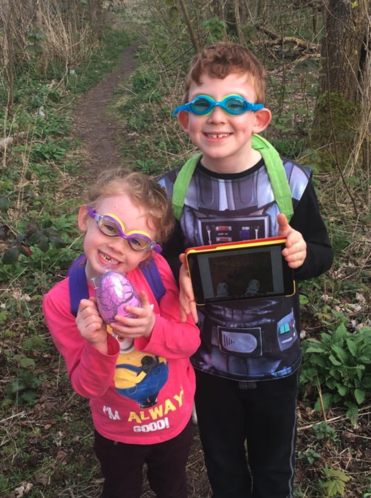 2 children wearing swimming goggles in a forest with an iPad and egg