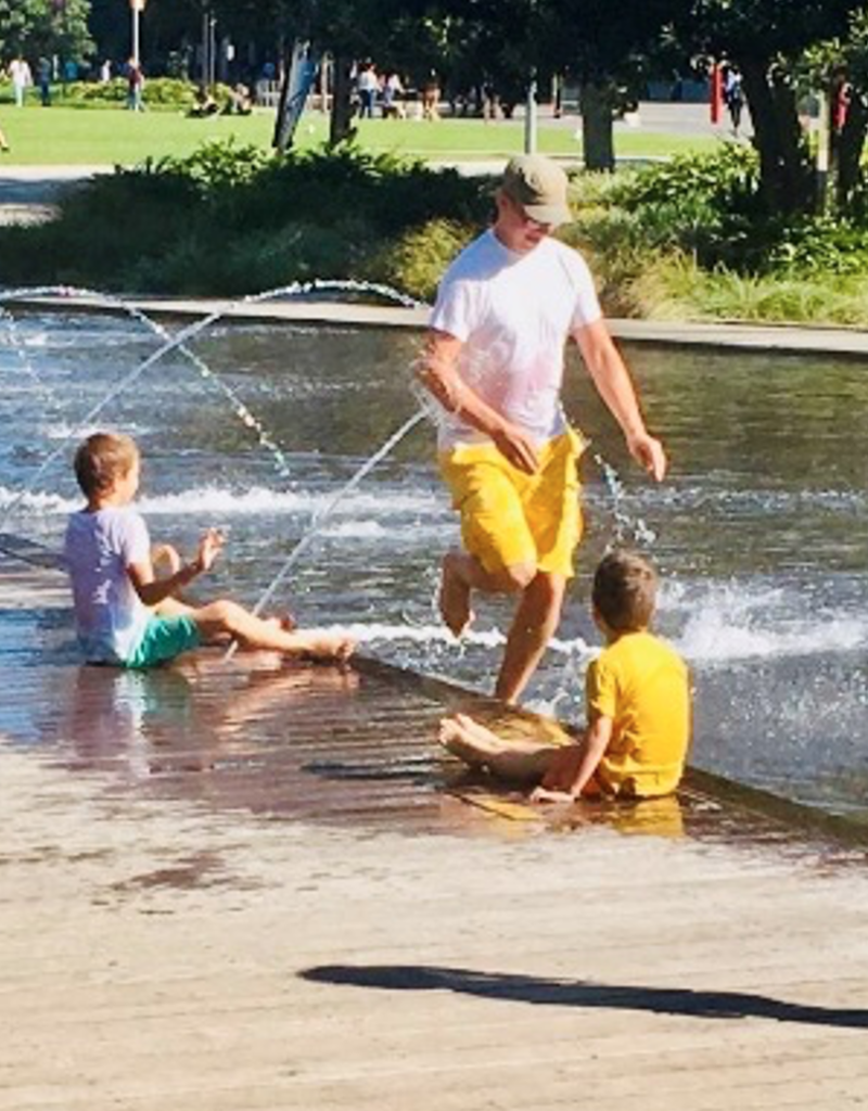 Man running through fountain with 2 children watching