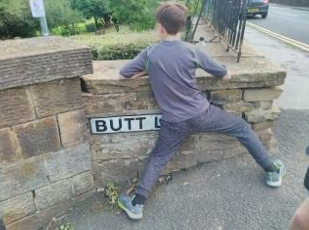 photo of boy covering road sign that says "Butt"
